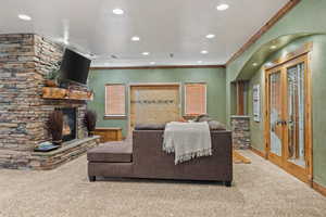 Carpeted living area featuring recessed lighting, a stone fireplace, and ornamental molding