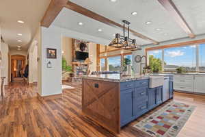 Kitchen featuring beamed ceiling, arched walkways, light wood-style floors, recessed lighting, and a stone fireplace