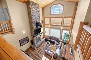 Living room featuring wood ceiling, high vaulted ceiling, wood finished floors, and a stone fireplace