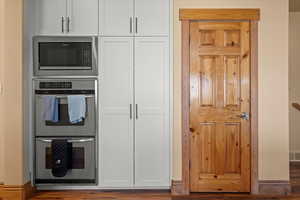 Kitchen featuring stainless steel double oven, white cabinetry, wood finished floors, built in microwave, and baseboards