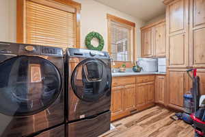 Clothes washing area featuring cabinet space, light wood-style flooring, and washer and dryer