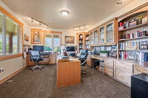 Office area featuring a textured ceiling, dark carpet, visible vents, and a healthy amount of sunlight