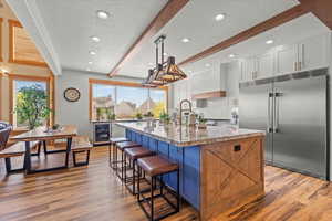 Kitchen with light stone counters, built in fridge, a kitchen island, white cabinets, and pendant lighting