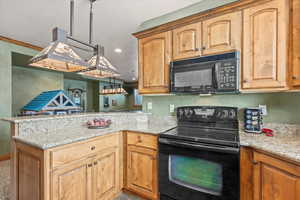 Kitchen with light stone counters, recessed lighting, a peninsula, baseboards, and black appliances