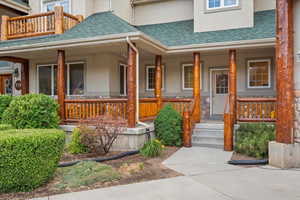 View of exterior entry with a shingled roof, a porch, and stucco siding