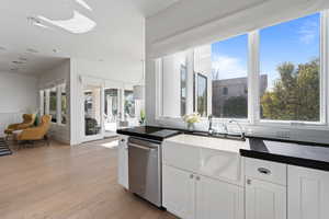 Kitchen featuring sink, tasteful backsplash, light wood-type flooring, stainless steel dishwasher, and white cabinets