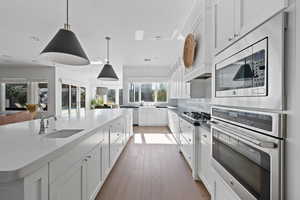 Kitchen featuring sink, white cabinets, hanging light fixtures, a kitchen island with sink, and stainless steel appliances