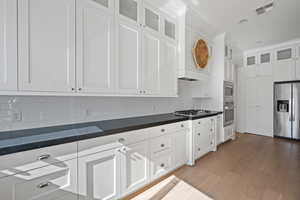 Kitchen with hardwood / wood-style flooring, appliances with stainless steel finishes, white cabinets, and decorative backsplash