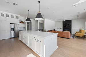 Kitchen with white cabinetry, a center island, stainless steel fridge with ice dispenser, hanging light fixtures, and light hardwood / wood-style flooring