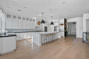 Kitchen with white cabinetry, decorative light fixtures, light wood-type flooring, appliances with stainless steel finishes, and a kitchen island