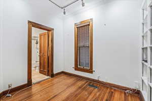 Empty room with crown molding, wood-type flooring, and rail lighting