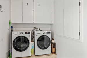 Clothes washing area featuring washing machine and dryer and cabinets