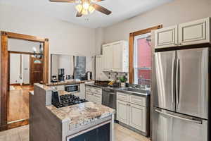 Kitchen with appliances with stainless steel finishes, white cabinetry, sink, ceiling fan, and light stone counters