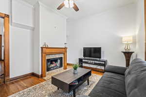 Living room with crown molding, ceiling fan, wood-type flooring, and a fireplace