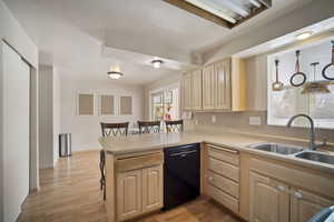 Kitchen featuring light countertops, light brown cabinets, a sink, dishwasher, and a peninsula