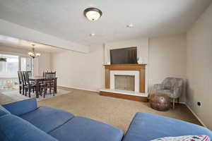 Carpeted living area with a fireplace with raised hearth, a textured ceiling, baseboards, and an inviting chandelier