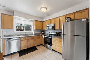 Kitchen featuring light tile patterned floors, visible vents, appliances with stainless steel finishes, stone countertops, and a sink