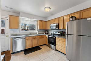 Kitchen with stone counters, light tile patterned flooring, a sink, visible vents, and appliances with stainless steel finishes