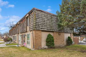 Exterior space with mansard roof, a lawn, fence, and brick siding