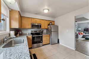 Kitchen with light stone counters, light tile patterned floors, stainless steel appliances, a sink, and baseboards