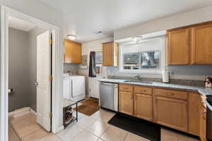 Kitchen with light tile patterned floors, visible vents, dishwasher, washing machine and clothes dryer, and a sink