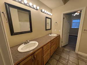 Bathroom featuring stone tile flooring, double vanity, baseboards, and a sink