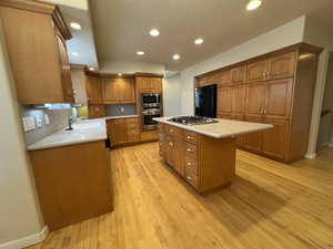 Kitchen featuring appliances with stainless steel finishes, brown cabinets, a center island, light countertops, and a sink