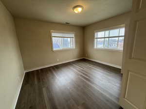 Empty room with visible vents, dark wood finished floors, a textured ceiling, and baseboards