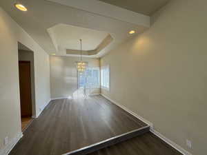 Unfurnished dining area with a tray ceiling, dark hardwood / wood-style flooring, and a notable chandelier