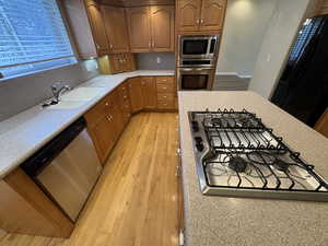 Kitchen featuring light countertops, appliances with stainless steel finishes, brown cabinetry, a sink, and light wood-type flooring