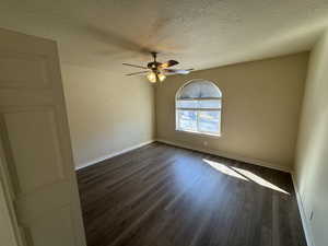 Empty room with ceiling fan, dark hardwood / wood-style flooring, and a textured ceiling