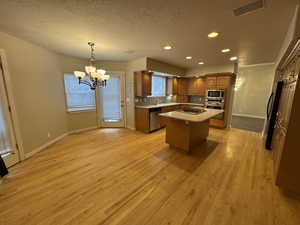 Kitchen featuring brown cabinets, a center island, stainless steel appliances, light countertops, and light wood-type flooring