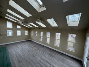 Unfurnished room featuring lofted ceiling, baseboards, and wood finished floors