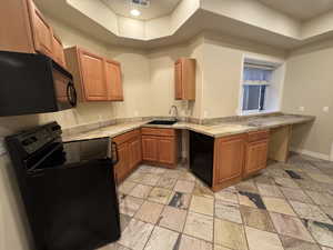 Kitchen featuring a raised ceiling, light countertops, brown cabinetry, a sink, and black appliances