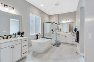 Bathroom with marble finish floor, two vanities, a freestanding bath, a stall shower, and a sink