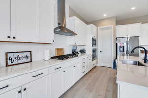 Kitchen featuring stainless steel appliances, a sink, white cabinets, wall chimney exhaust hood, and light wood finished floors