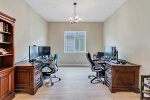 Office space with baseboards, light wood finished floors, and an inviting chandelier