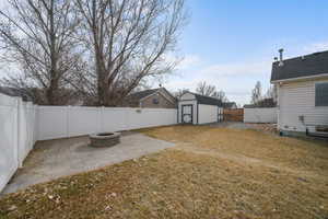 View of yard with a patio, a fenced backyard, a fire pit, an outdoor structure, and a storage unit