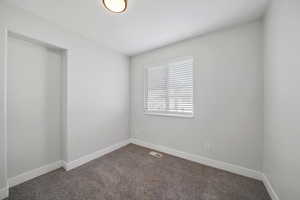 Spare room with dark carpet, visible vents, and baseboards