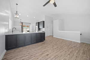 Kitchen featuring stainless steel fridge, light wood-style flooring, light countertops, pendant lighting, and a sink