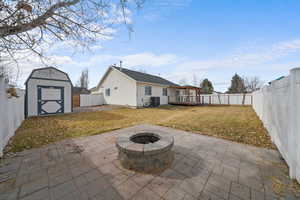 Rear view of property with a storage shed, central AC unit, a fire pit, a fenced backyard, and an outdoor structure