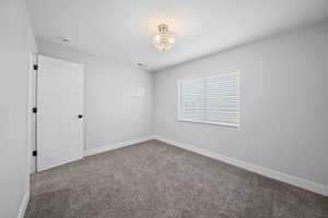 Unfurnished room featuring a textured ceiling, carpet flooring, visible vents, and baseboards