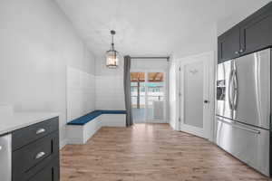 Interior space with stainless steel fridge, light countertops, light wood-style floors, pendant lighting, and a notable chandelier