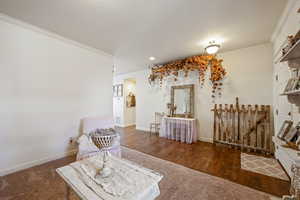 Living area with ornamental molding, dark wood-style flooring, dark carpet, and baseboards