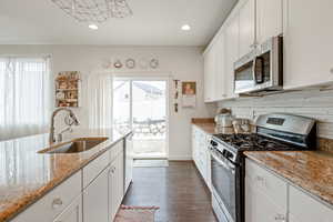 Kitchen featuring stainless steel appliances, a sink, white cabinets, and light stone countertops