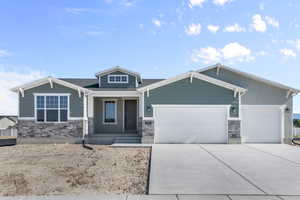 Craftsman inspired home featuring stone siding, a garage, a porch, and driveway