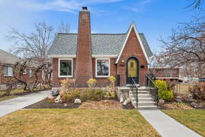 English style home with a shingled roof, brick siding, fence, a chimney, and a front yard