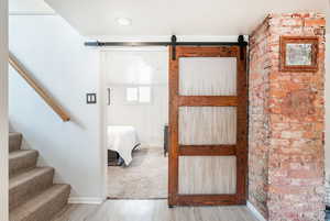 Interior space featuring brick wall, a barn door, light wood-style flooring, and baseboards