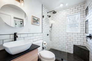 Bathroom featuring toilet, walk in shower, tile walls, and vanity