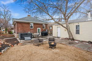 Back of house featuring a fire pit, brick siding, roof with shingles, a chimney, and a hot tub